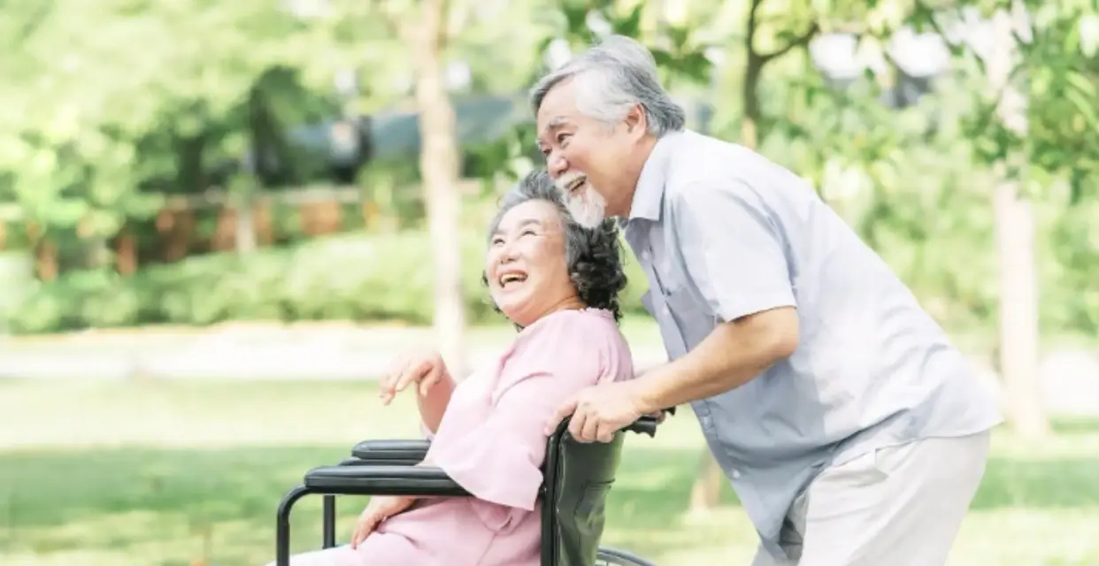 Elderly man assisting woman in wheelchair for mobility support in arthritis care