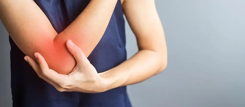 Woman holding her outer elbow  indicating symptoms of tennis elbow. 