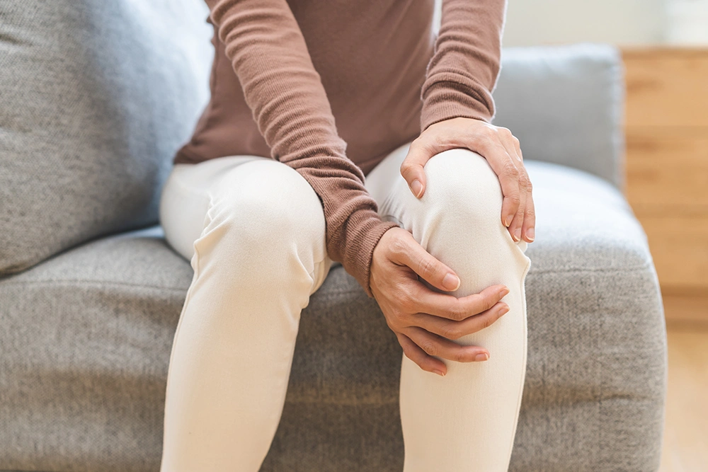Woman sitting down and holding her knee indicating knee pain.