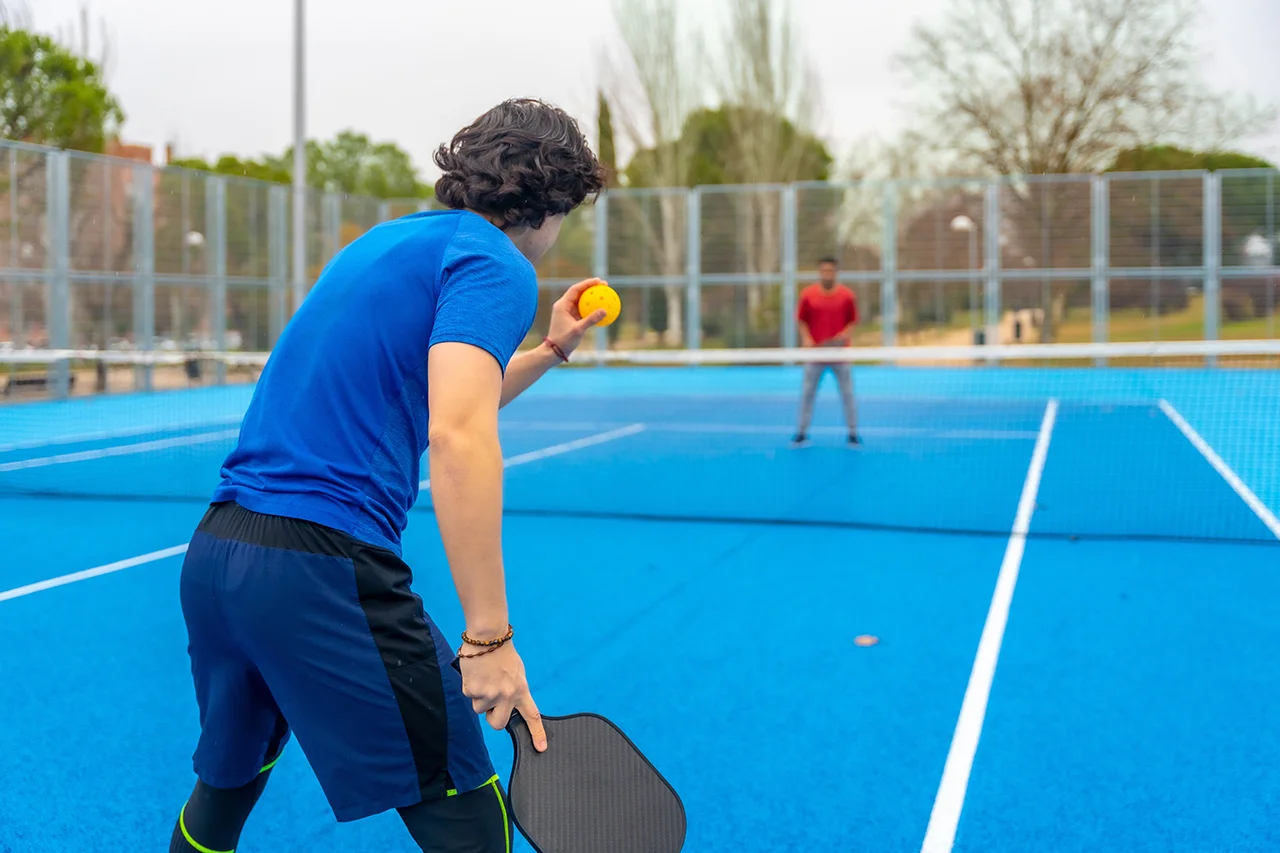 Pickleball player poised to serve on a blue outdoor court