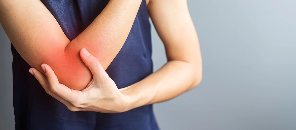 Woman holding her outer elbow indicating symptoms of tennis elbow.