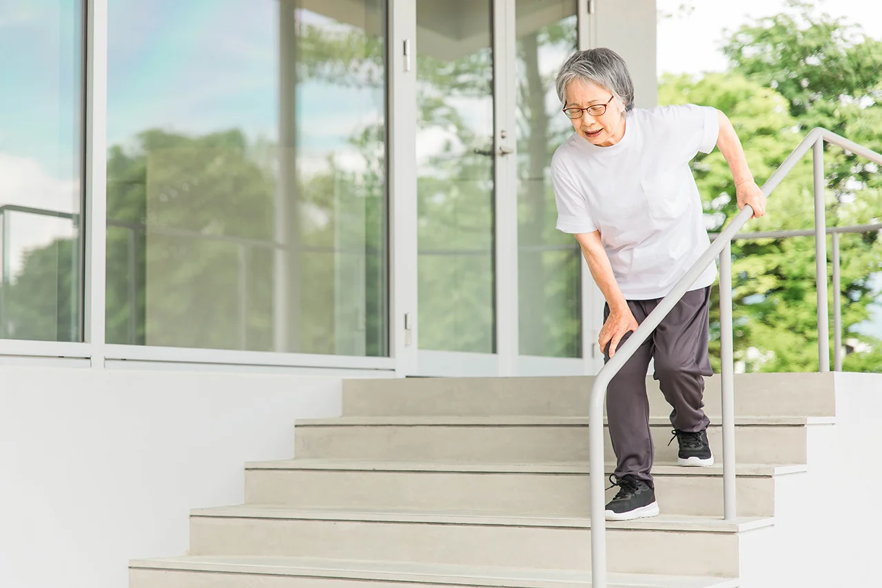 Woman experiencing knee discomfort while going down stairs.