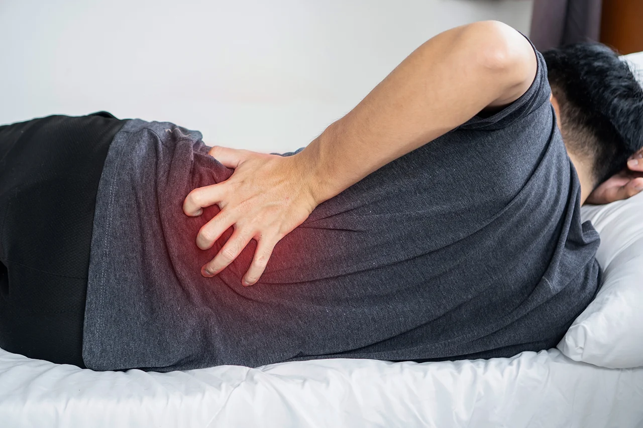Man lying on a bed while experiencing hip pain and discomfort.